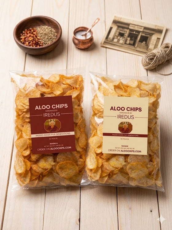 Two packages of Aloo Chips on a wooden surface with seasonings and a newspaper in the background.